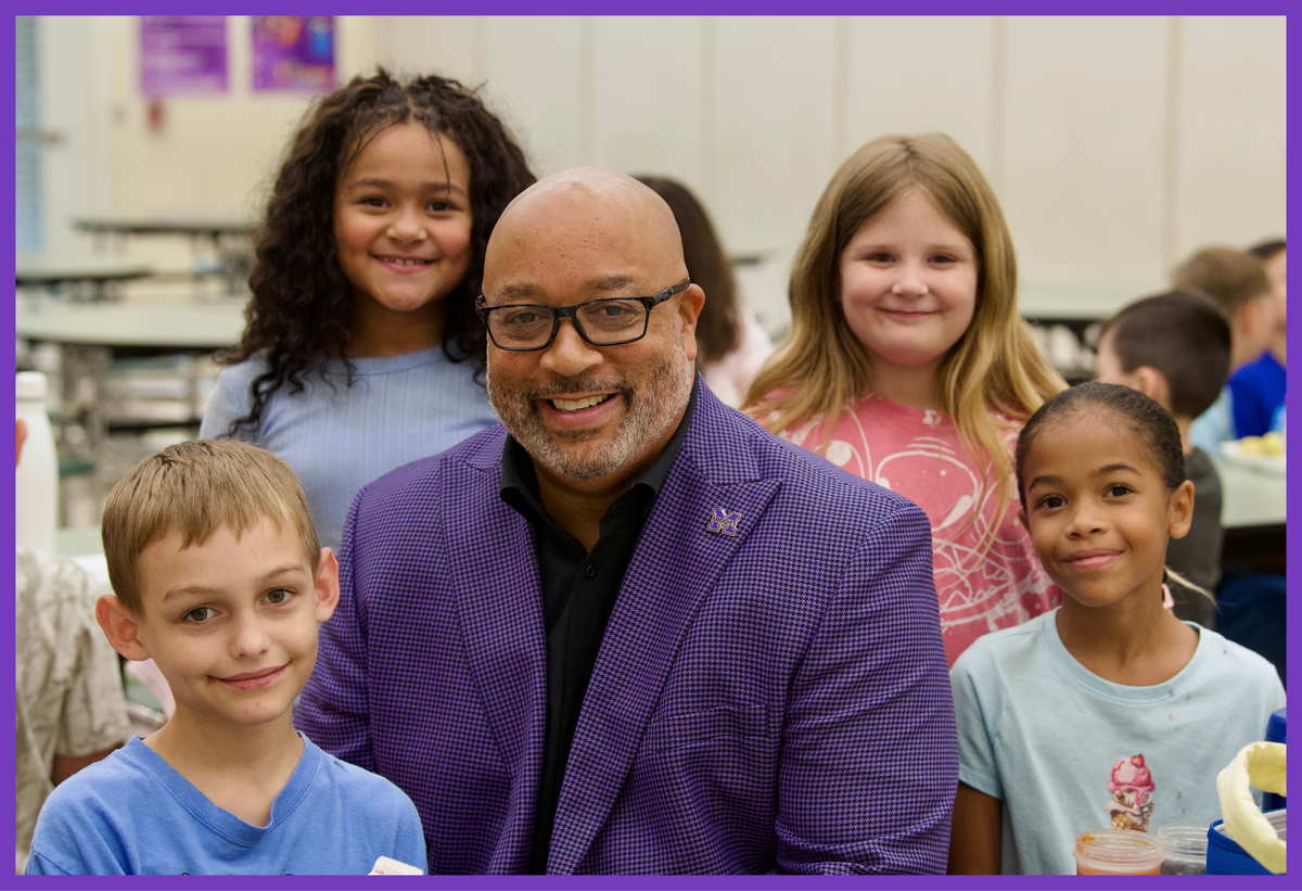 Superintendent Card sitting in the cafeteria with elementary students